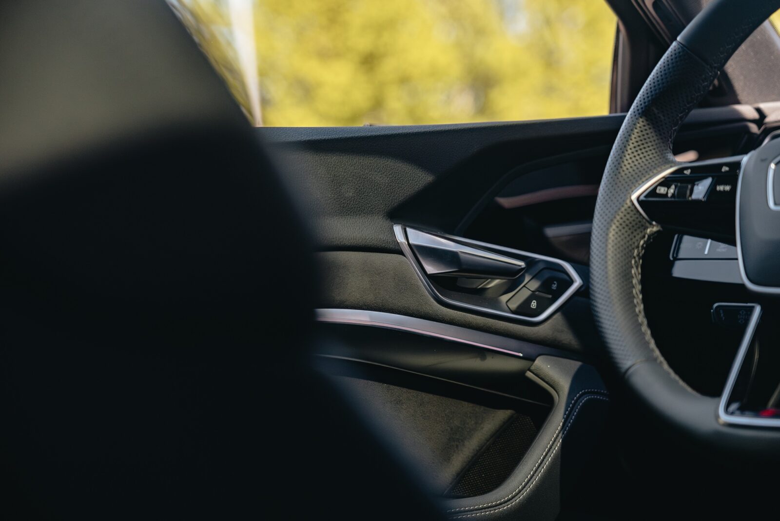 Close-up of a car's driver-side interior, showing the perforated steering wheel and control panel near the door.
